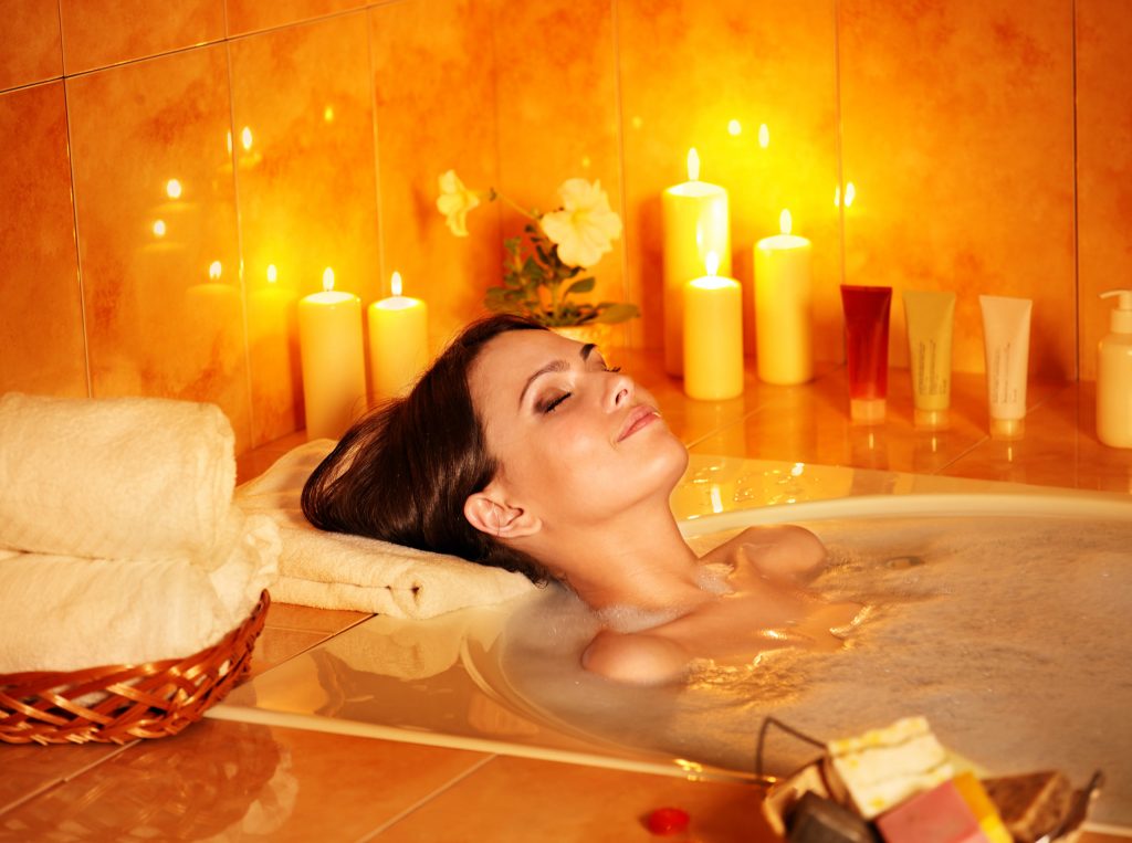 Frau liegt entspannt mit Kerzen in der Badewanne.